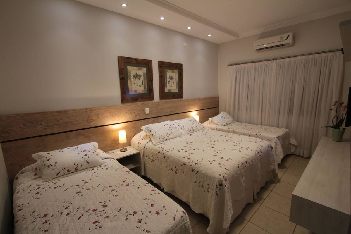 A hotel room with two single beds, a wooden headboard, an air conditioning unit, and a bedside table with a lamp.