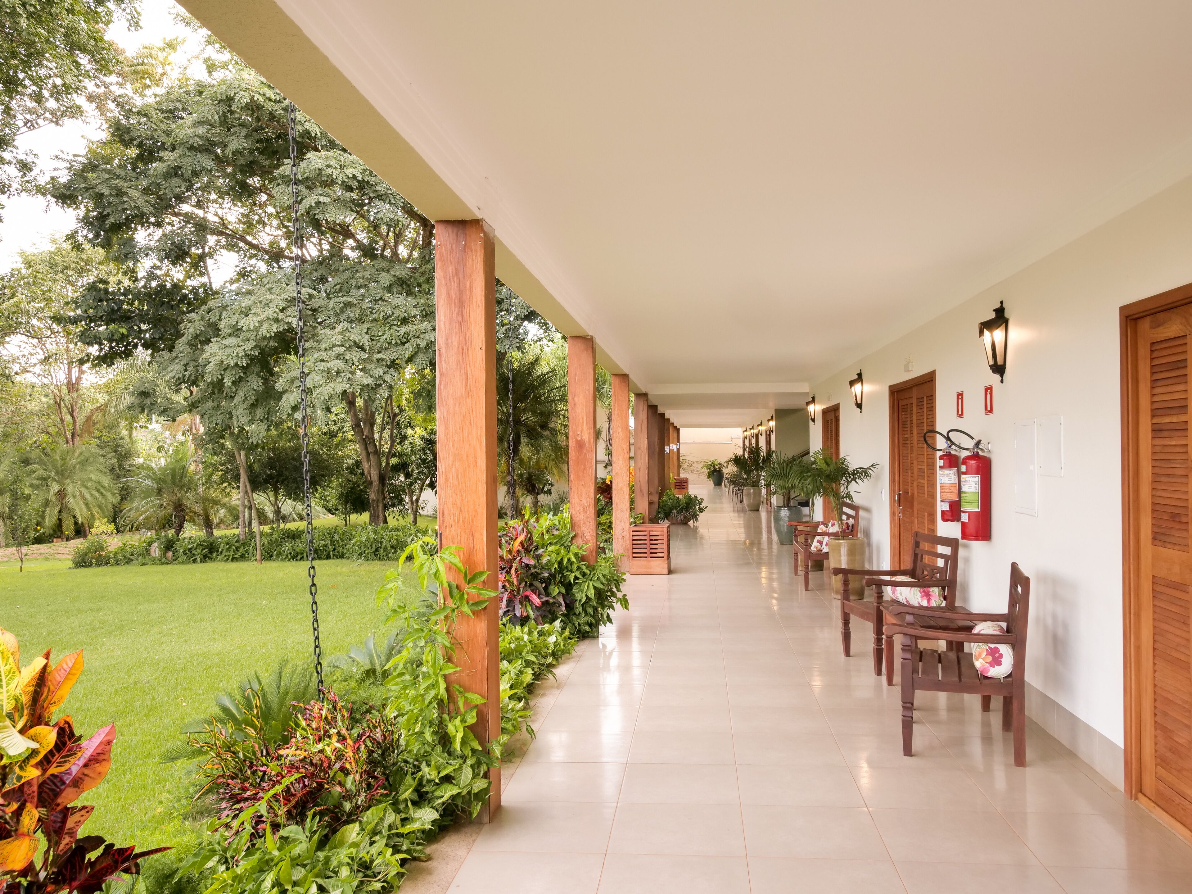 A covered corridor with wooden pillars, potted plants, and fire extinguishers on the wall.