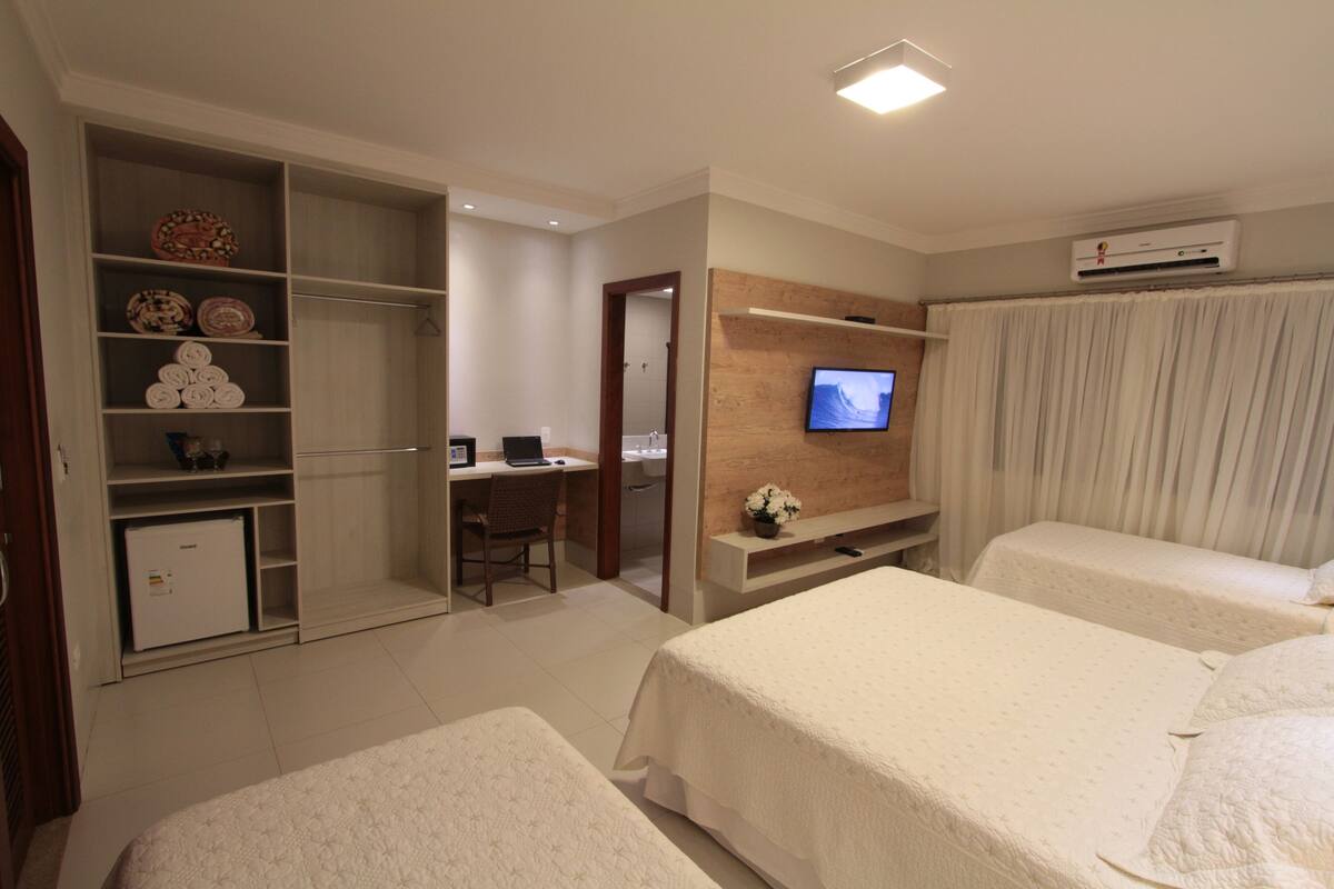 A hotel room with two beds, a desk with a chair, a television, and a wardrobe with shelves.