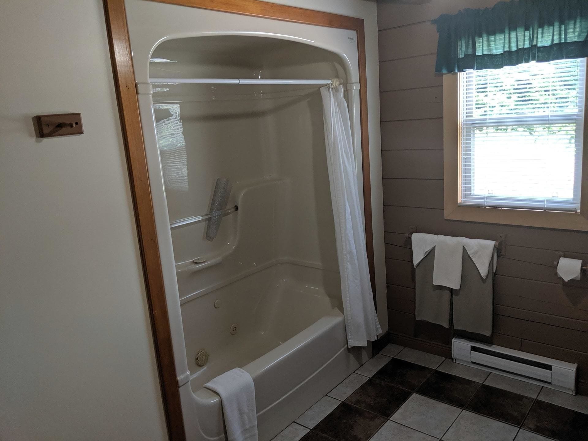 Un baño con bañera, cortina de ducha, ventana con persianas y radiador.