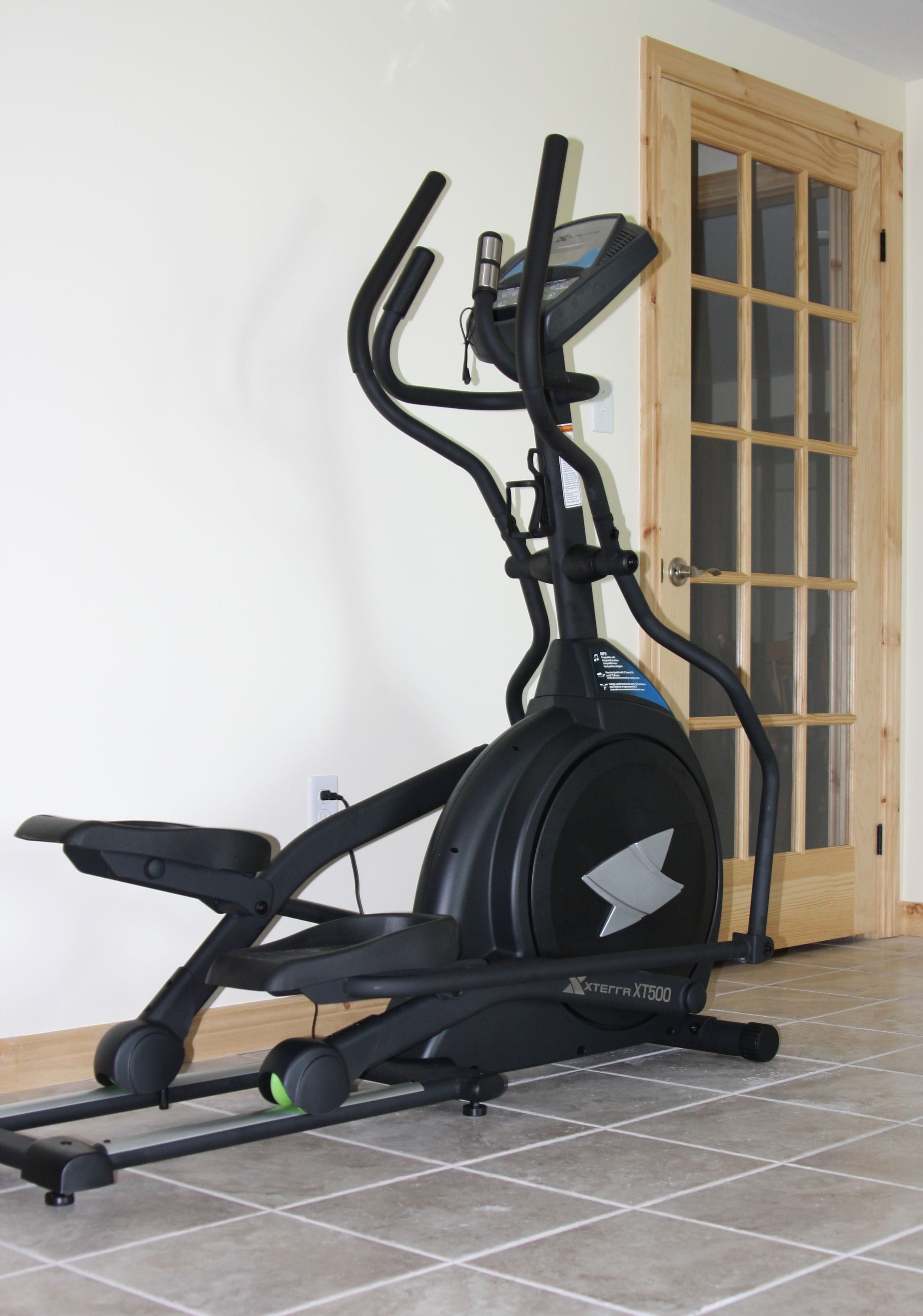 A stationary exercise bike in a room with a tiled floor and a wooden door with glass panels.
