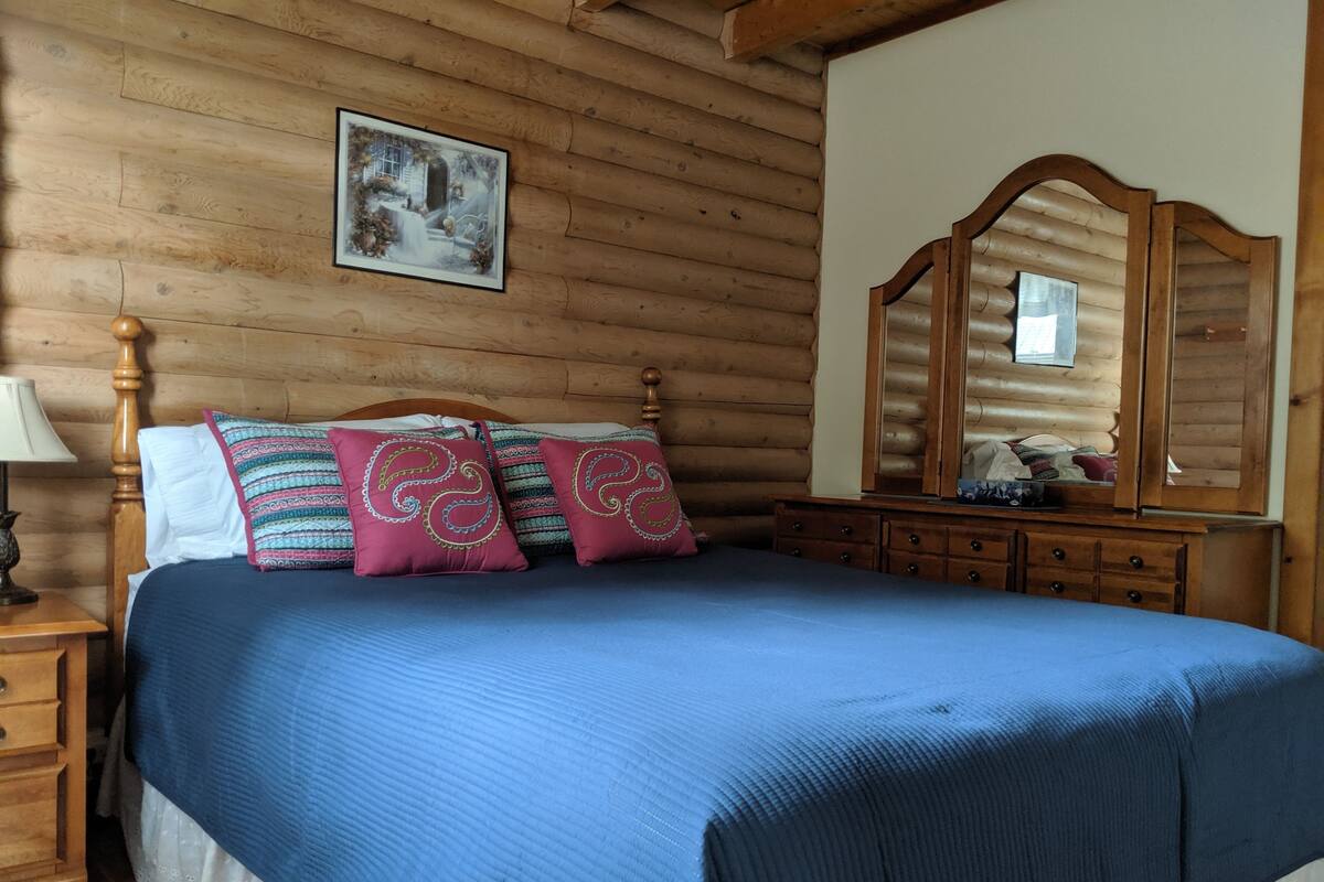 Ein Schlafzimmer in einer Holzhütte mit einem Bett, Kissen, einem Schminktisch und einem Spiegel.