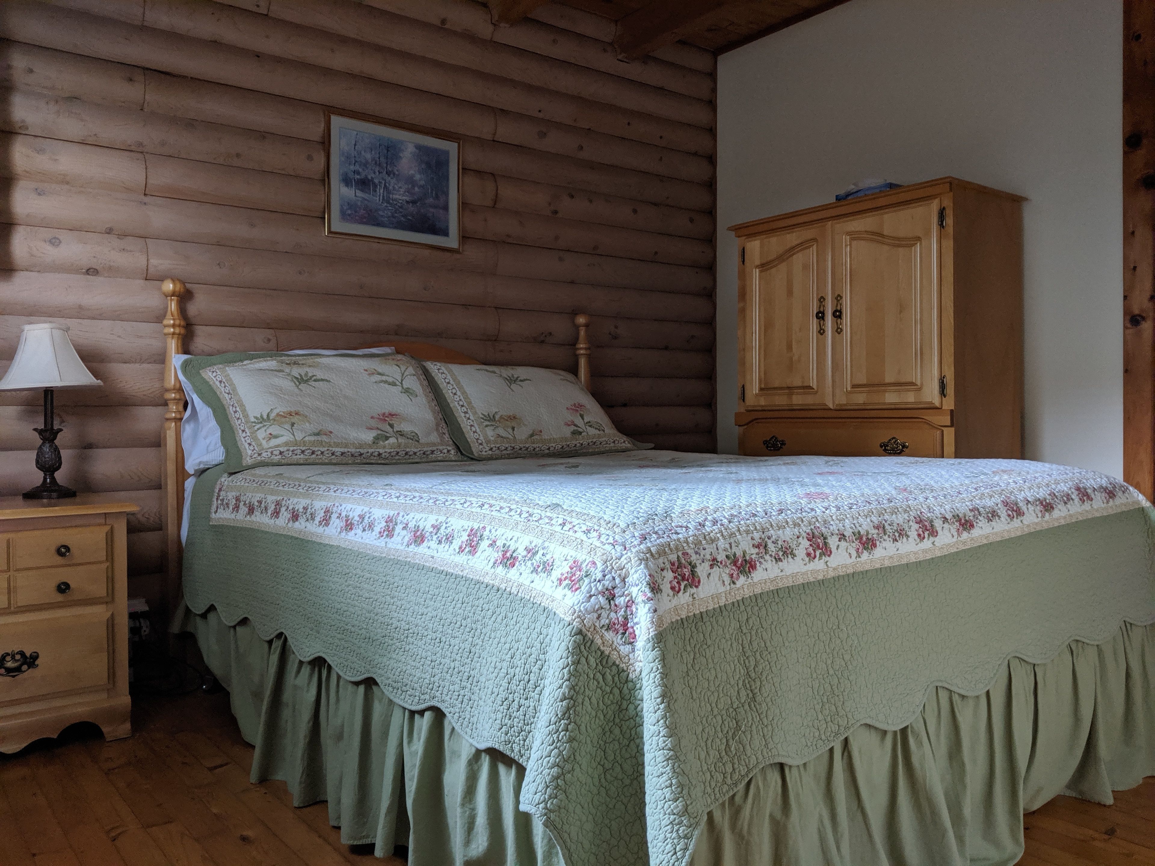 A wooden cabin bedroom with a bed, a nightstand, a lamp, and a wooden cabinet.
