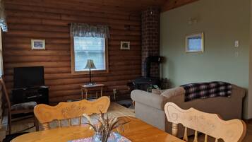 A cozy log cabin interior with a dining table, chairs, a sofa, a television, a fireplace, and framed pictures on the walls.