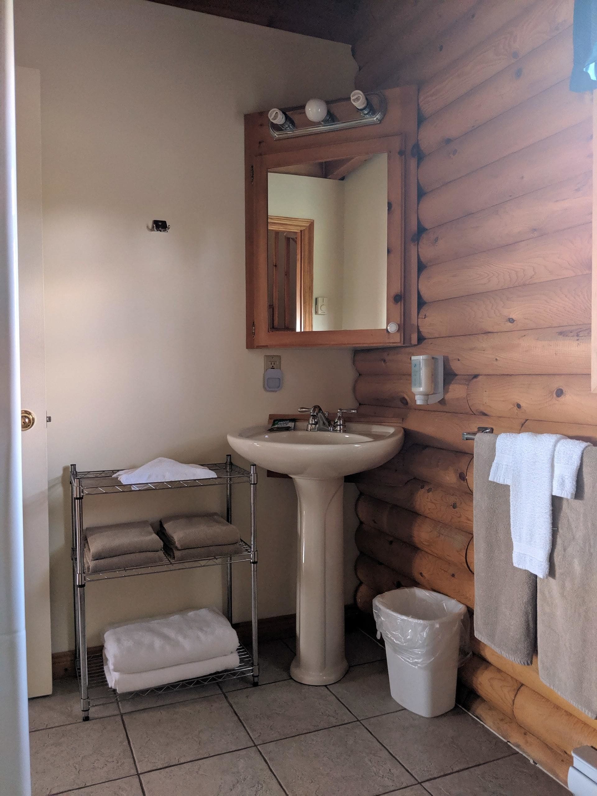 Een badkamer met een wastafel, spiegel, handdoekrek en een houten wand.