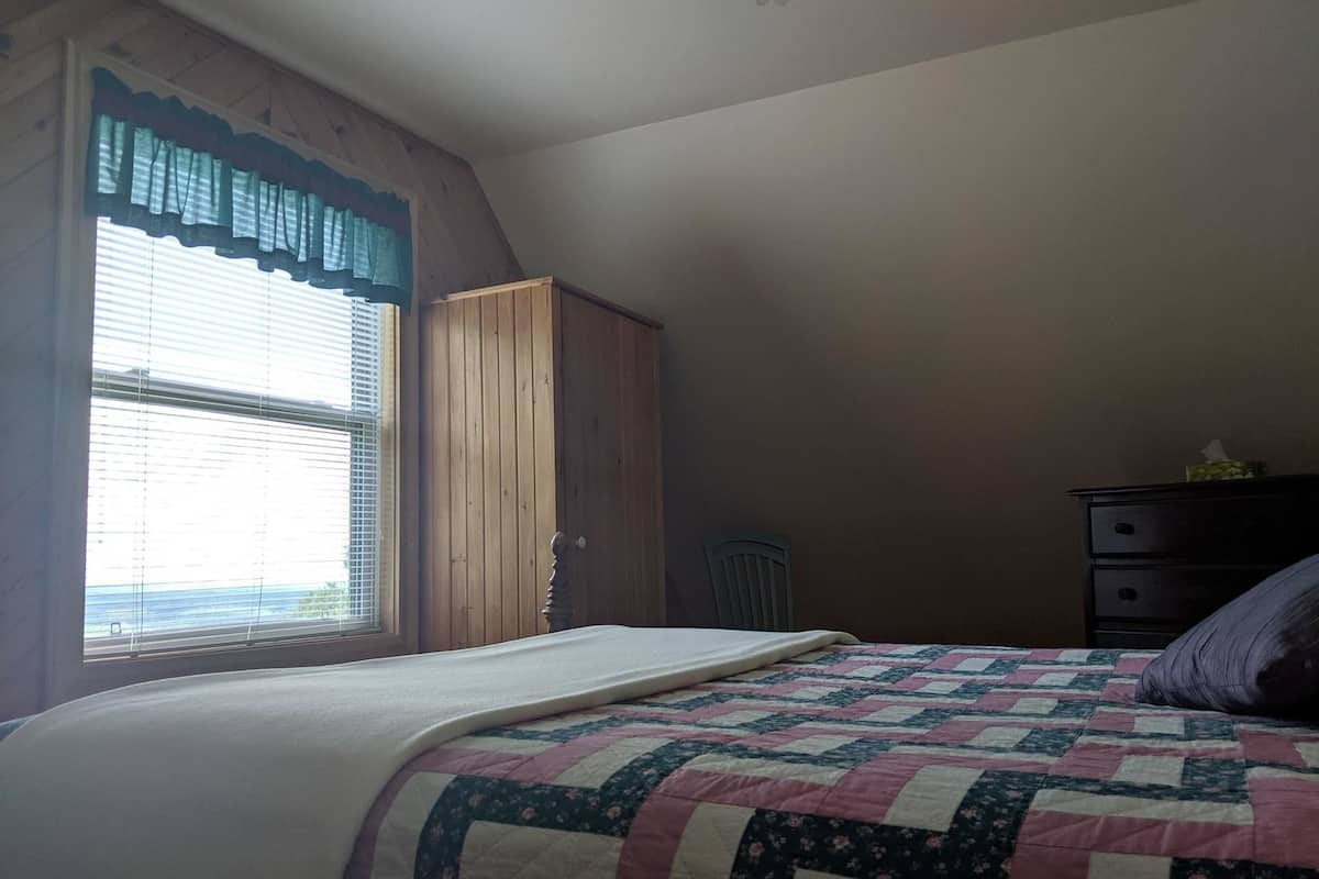Ein Schlafzimmer mit einem Bett, einem Fenster mit Jalousien, einem Holzschrank und einer Kommode.
