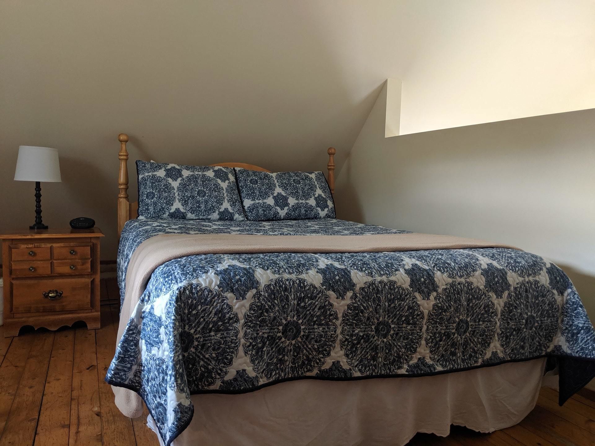 Una camera da letto con un letto di legno, un comodino con una lampada e una coperta a motivi.