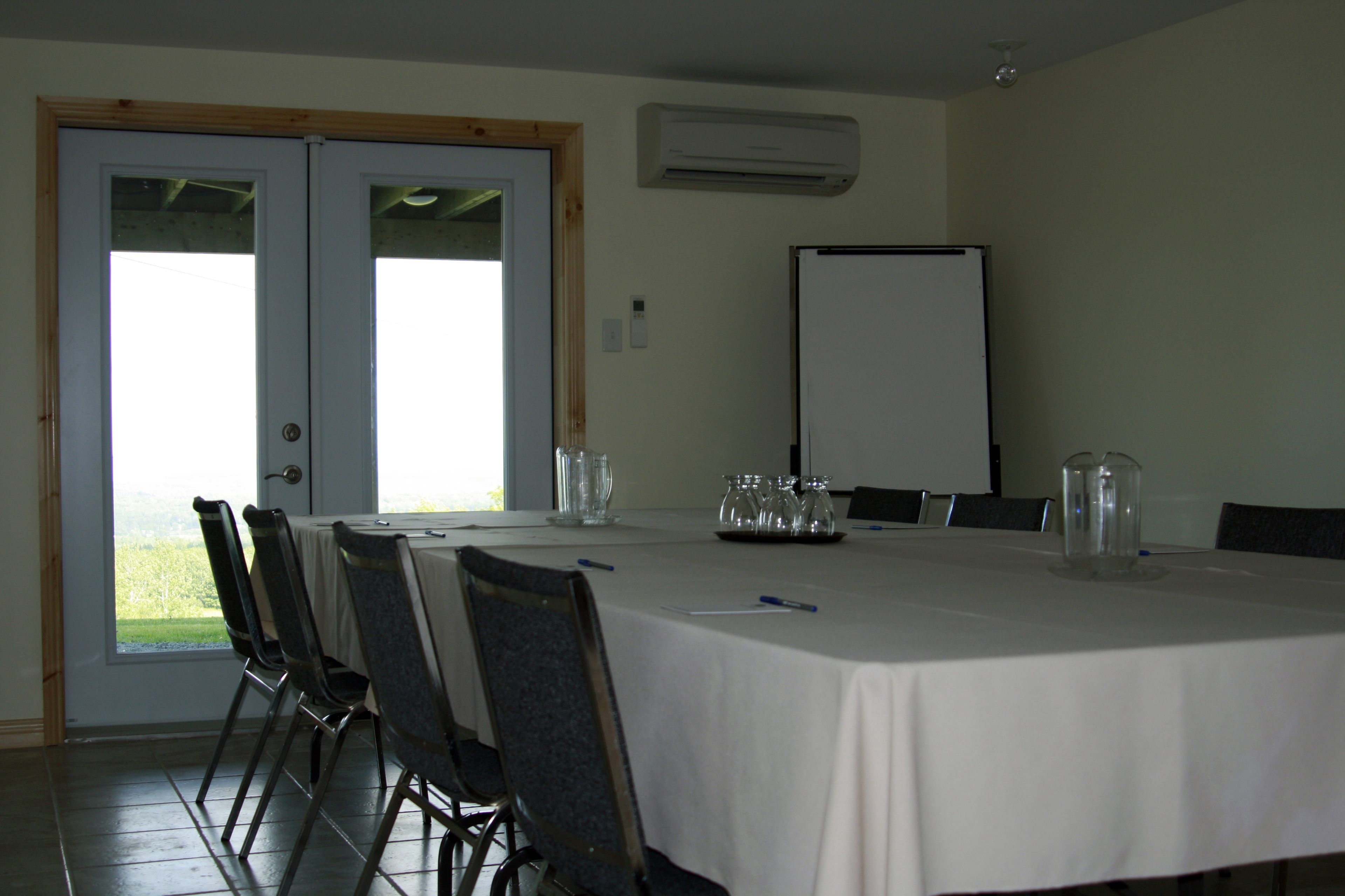 Une salle de conférence avec une table blanche, des chaises, un tableau blanc et une porte donnant sur un balcon.