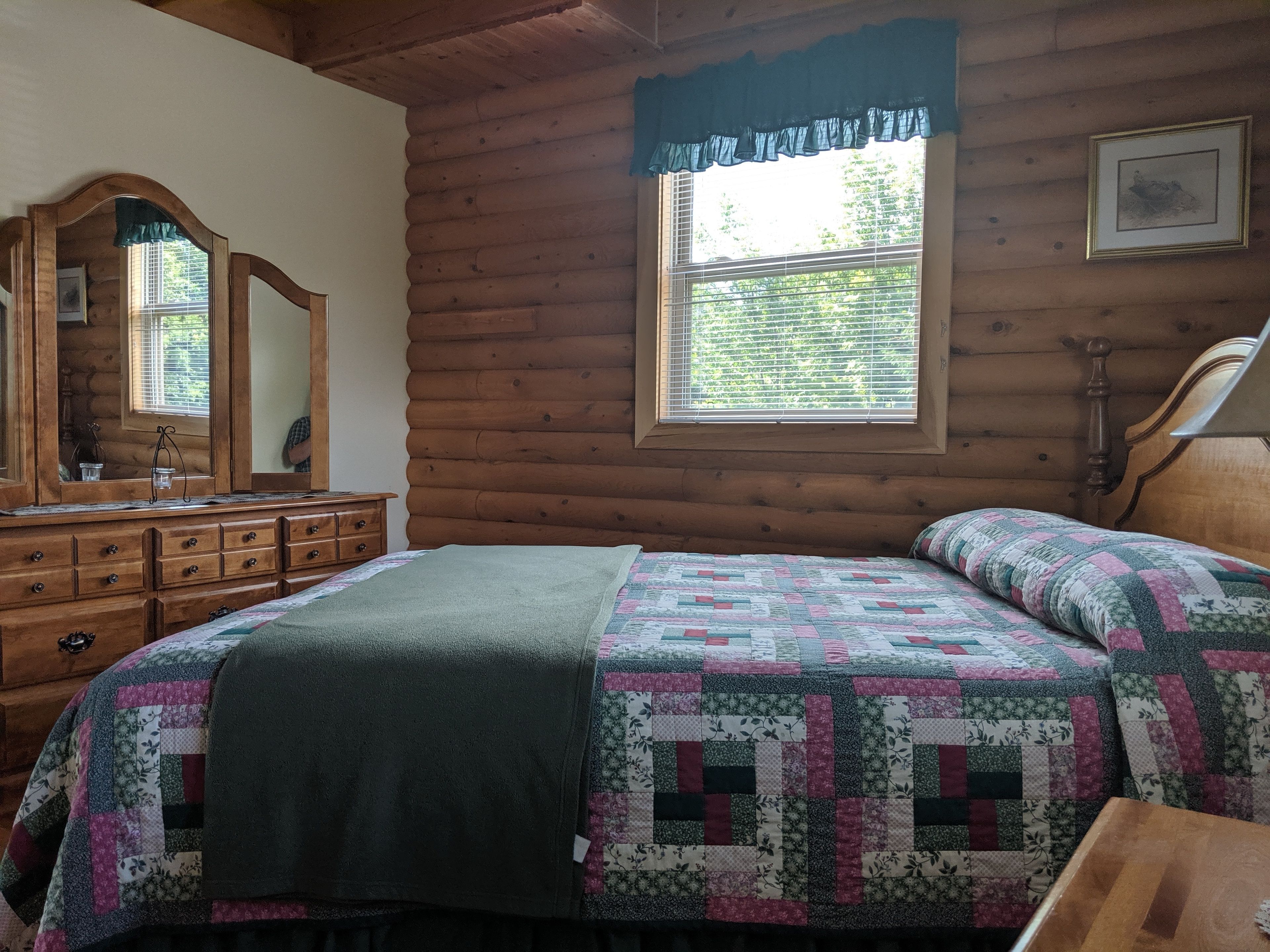 Un dormitorio tipo cabaña de troncos con cama, cómoda, espejo y ventana.