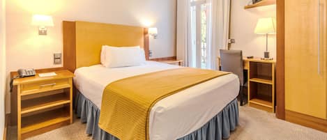 Hotellihuone, jossa on sänky, yöpöydät, työpöytä, tuoli, televisio ja ikkuna, jossa on verhot.
