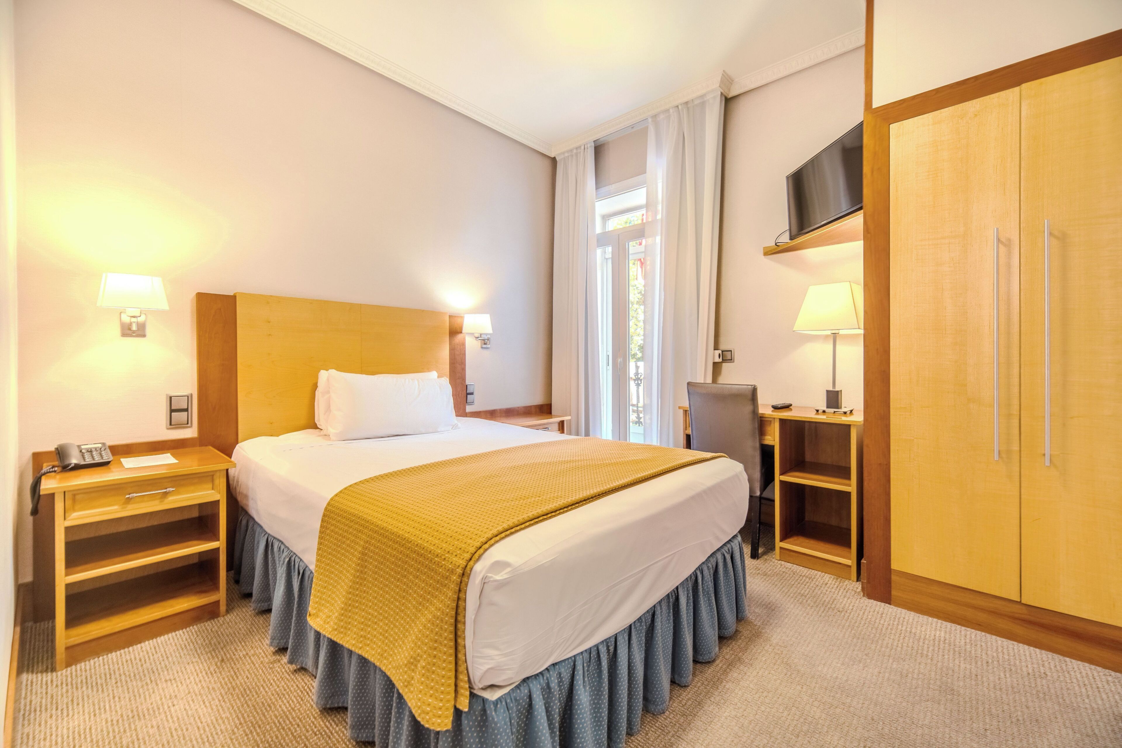 A hotel room with a bed, bedside tables, a desk, a wardrobe, and a TV.