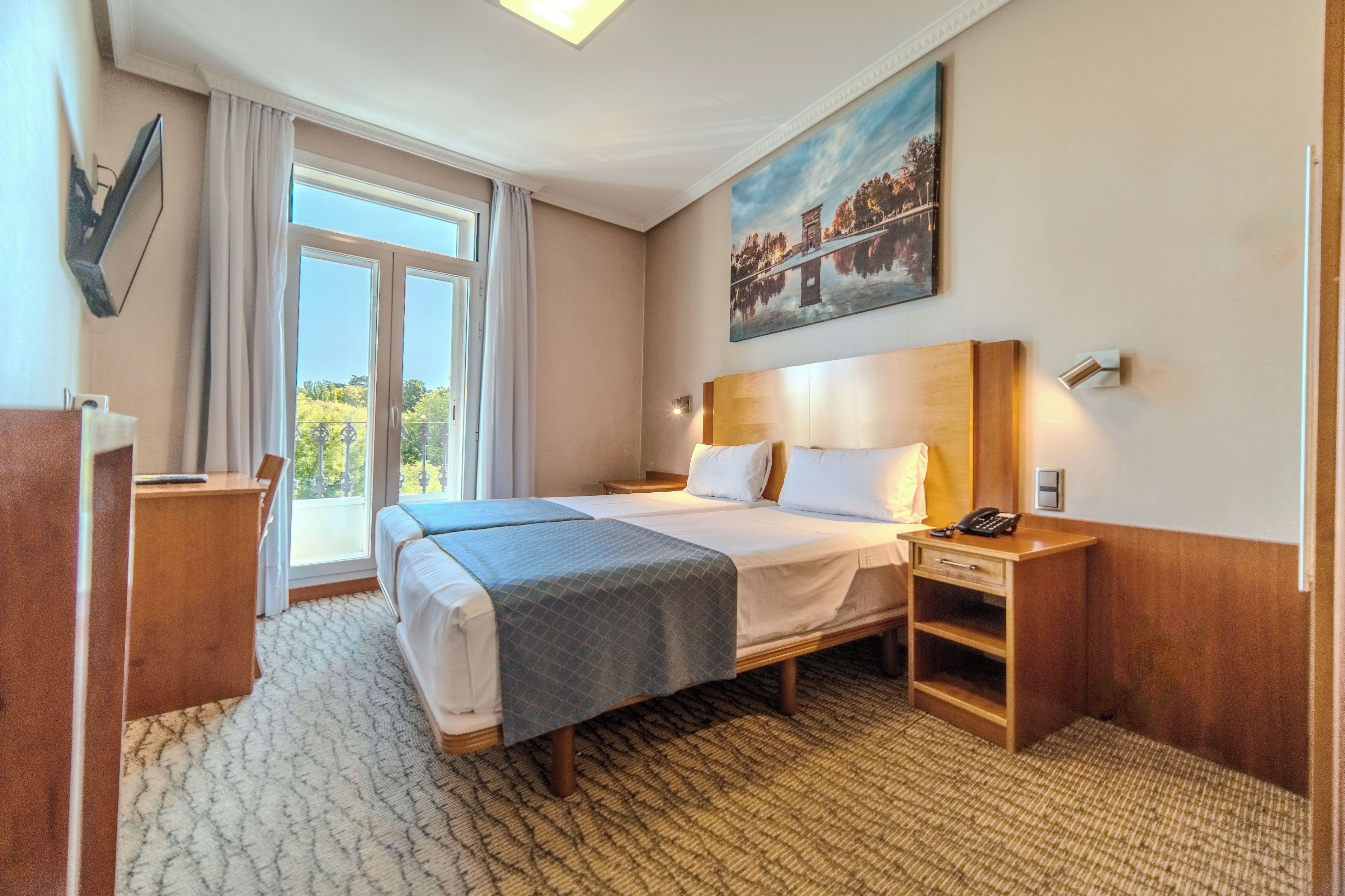 A hotel room with a bed, a desk, a telephone, and a painting on the wall.