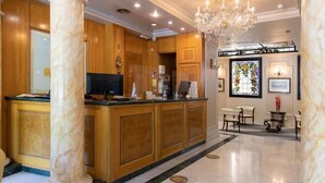 A hotel lobby with a reception desk, wooden paneling, a chandelier, and a seating area with tables and chairs. - ITC Mora by Soho Boutique (Madrid)