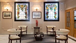 A lobby with four upholstered chairs, a central table, and two stained glass windows with floral designs. - ITC Mora by Soho Boutique (Madrid)