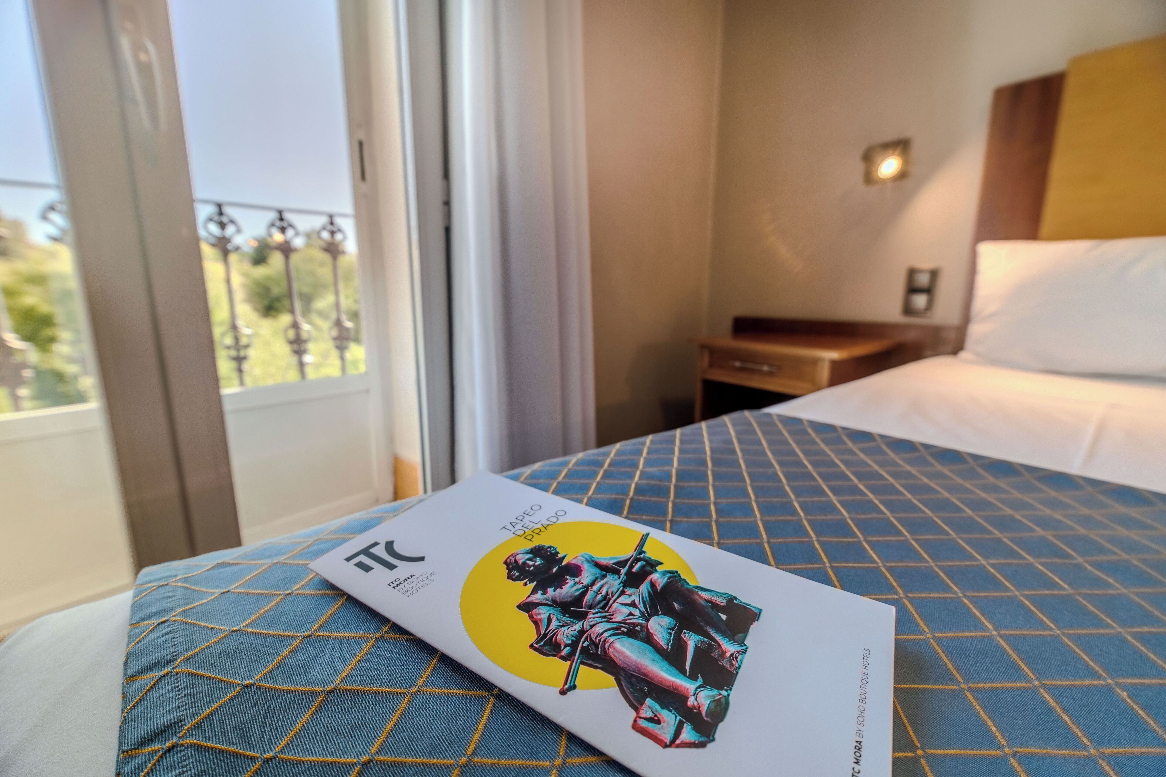 A hotel room with a bed, a nightstand, and a window with a view of greenery.