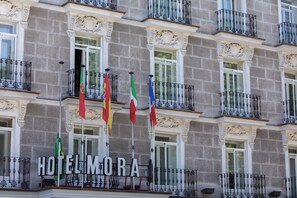 Ein Hotel mit Fassade, mehreren Balkonen, Flaggen und einem Schild mit der Aufschrift 'HOTEL MORA'.