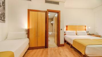 Een hotelkamer met twee bedden, houten vloeren, een kledingkast en een badkamer zichtbaar door een geopende deur.