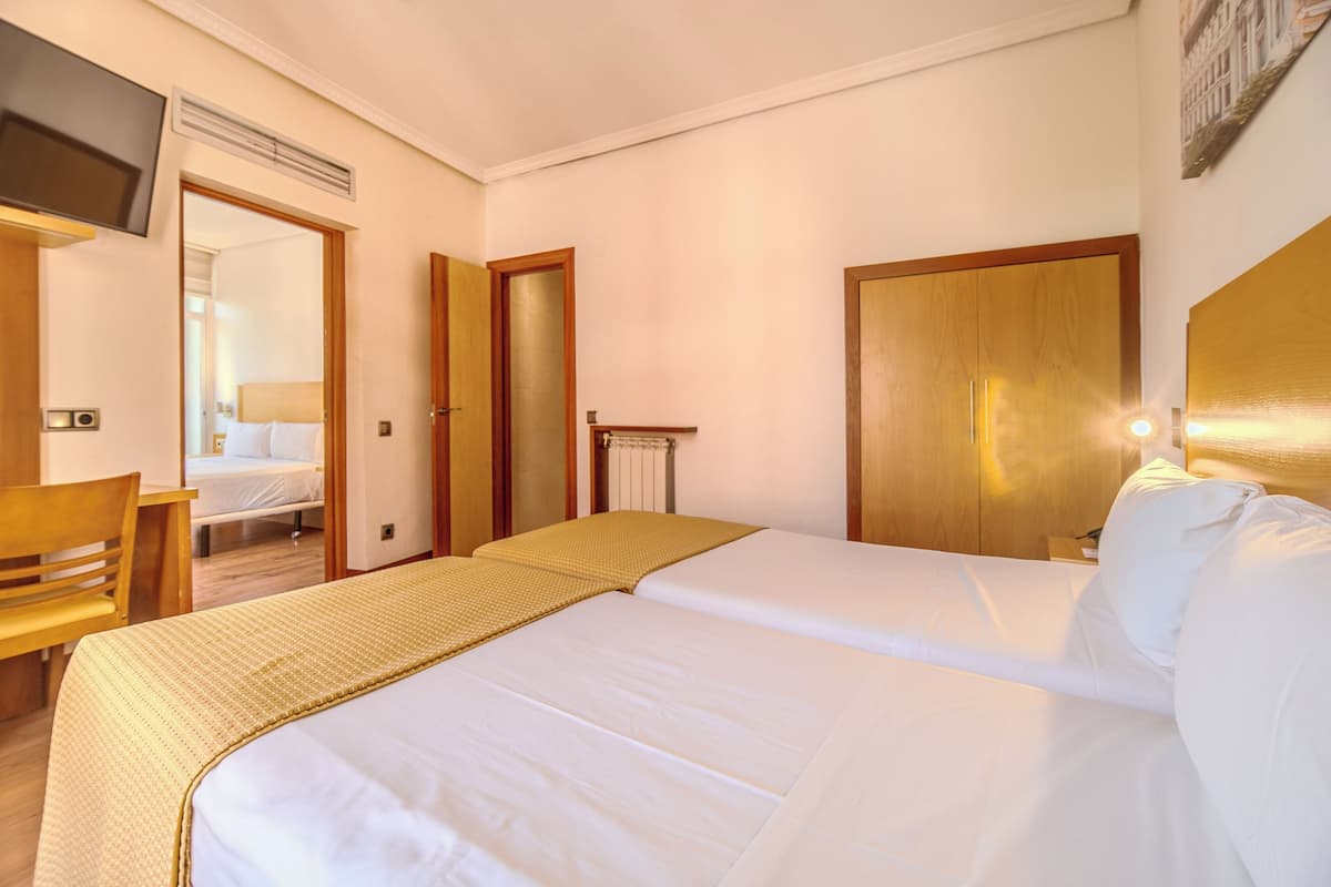 A hotel room with a bed, a desk, a chair, a television, and a wardrobe.