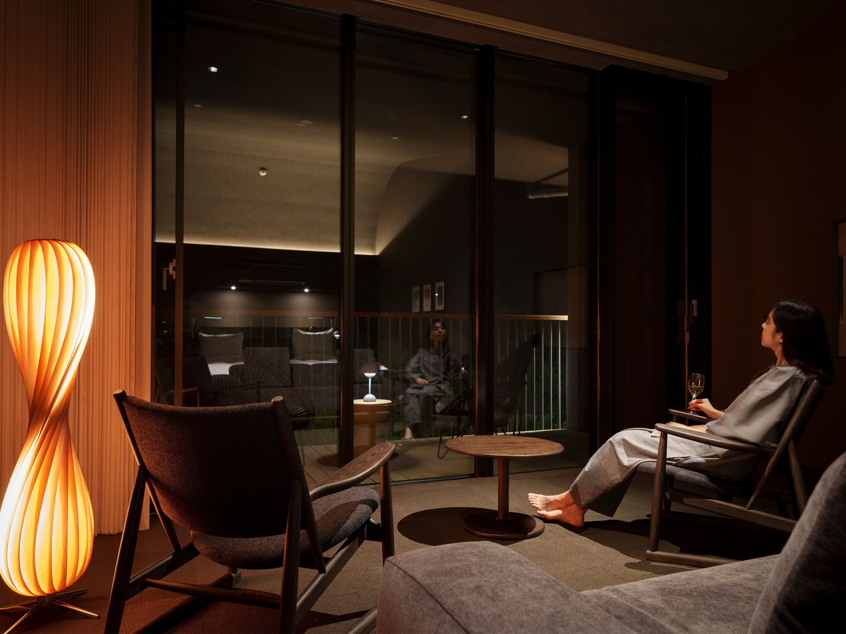 A modern hotel room with a large window, a sofa, a chair, and a floor lamp.