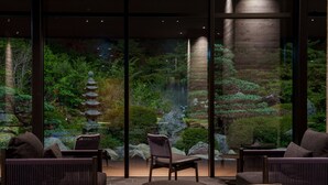 A serene indoor garden with a traditional Japanese pagoda, seating area, and a view of a lush landscape through large windows. - Unzen Miyazaki Ryokan (Unzen)