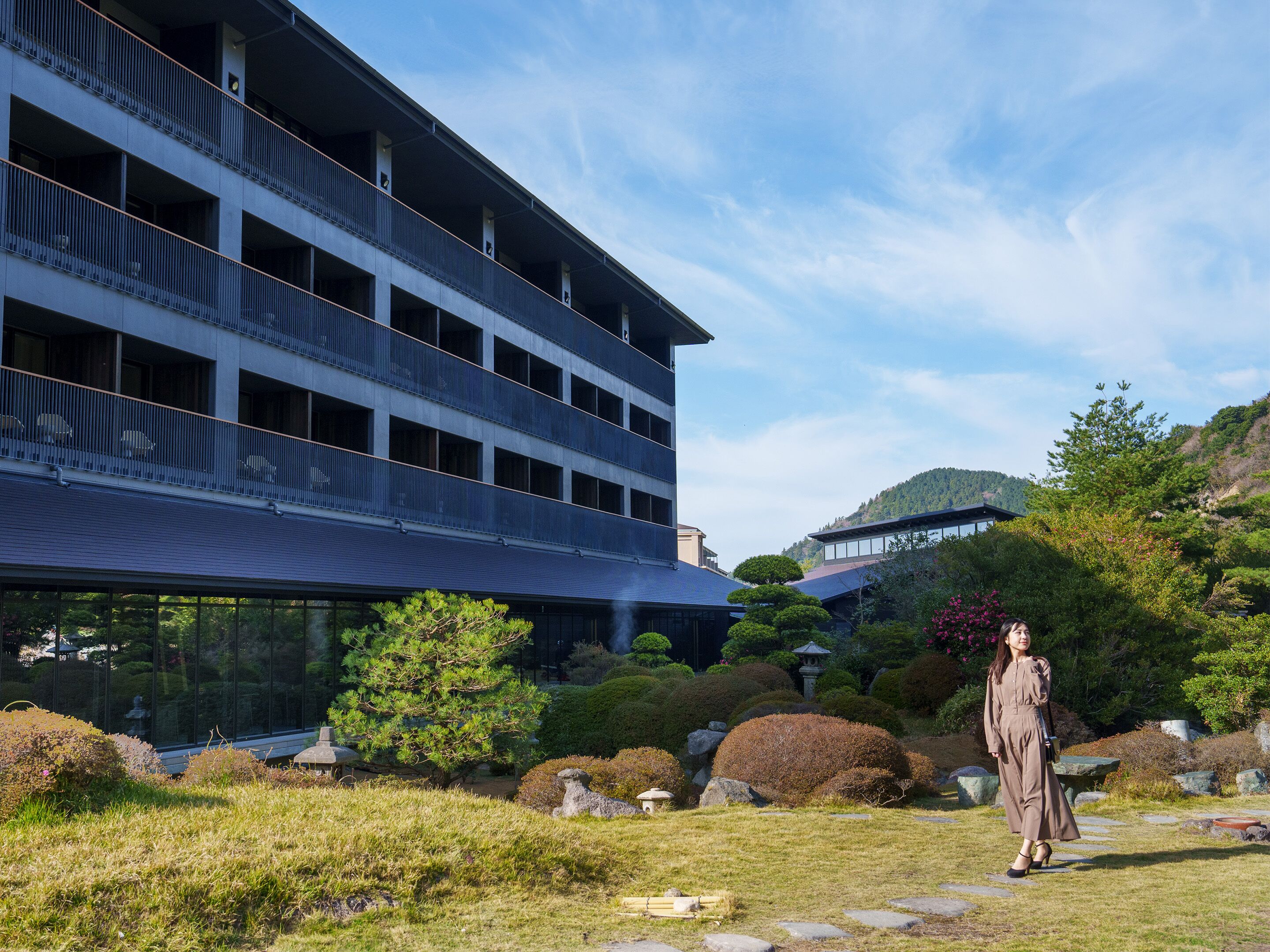 A modern building with multiple balconies and a garden area with various plants and rocks.