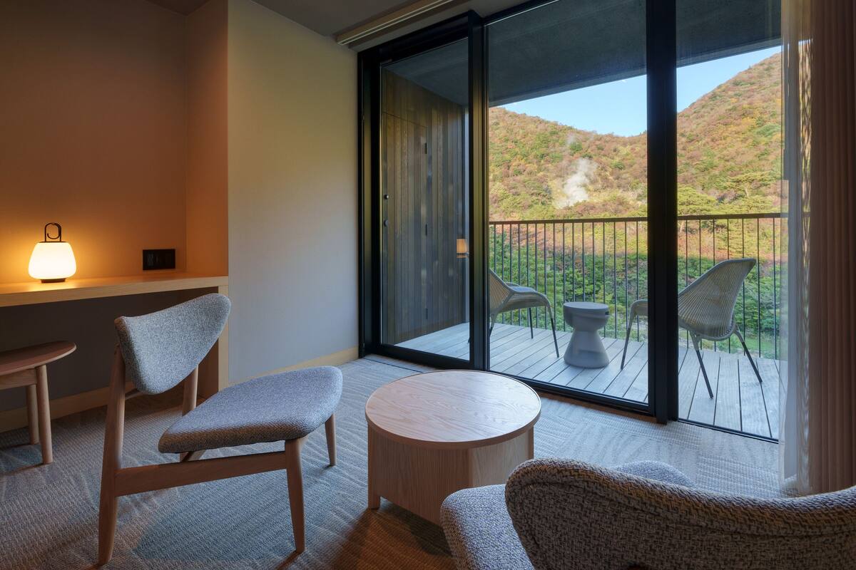 A balcony with a view of a hillside, furnished with two chairs and a small table.