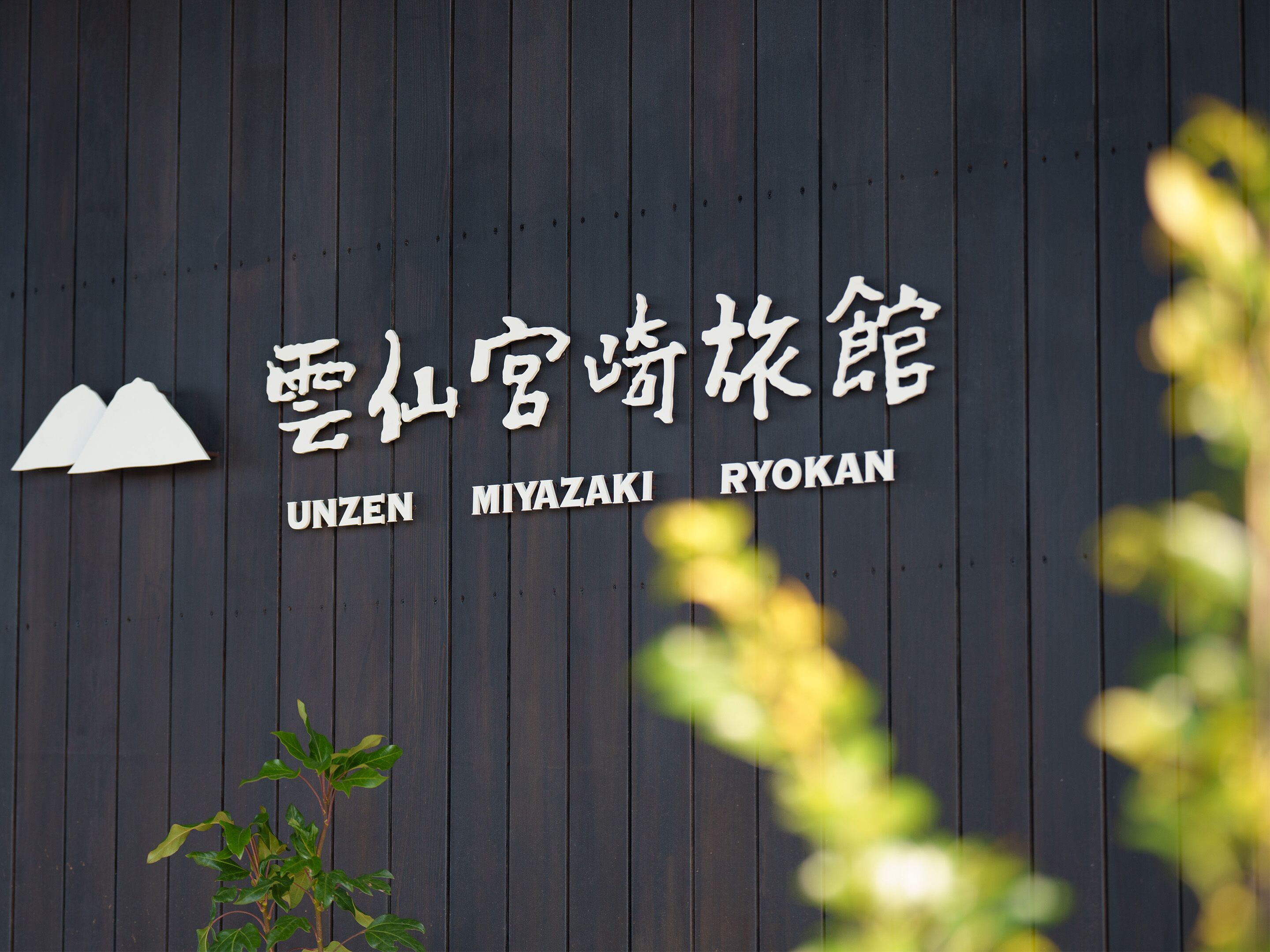 A sign with the name "UNZEN MIYAZAKI RYOKAN" on a wooden wall.
