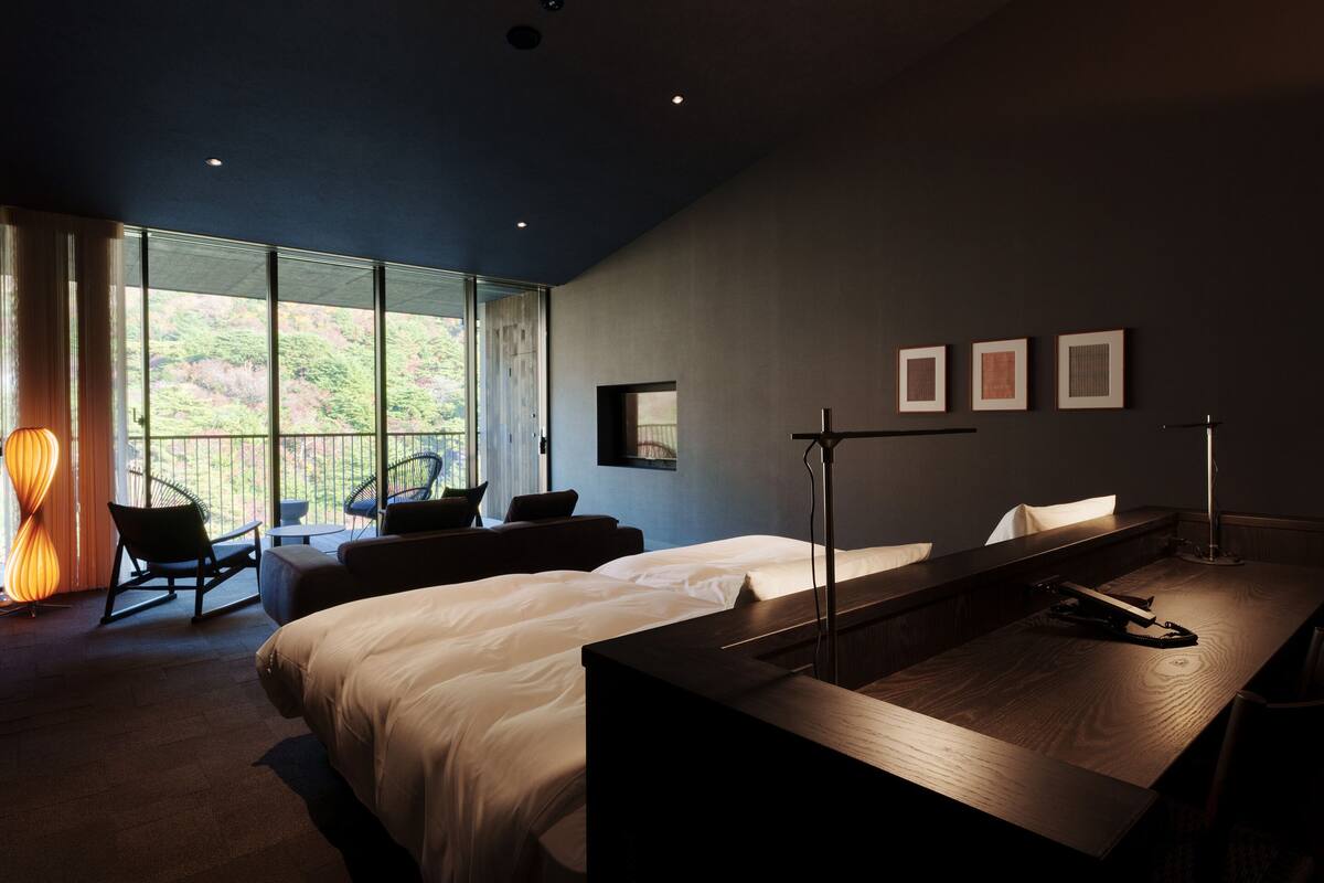 A modern hotel room with a large bed, a desk, and a balcony with a view of greenery.