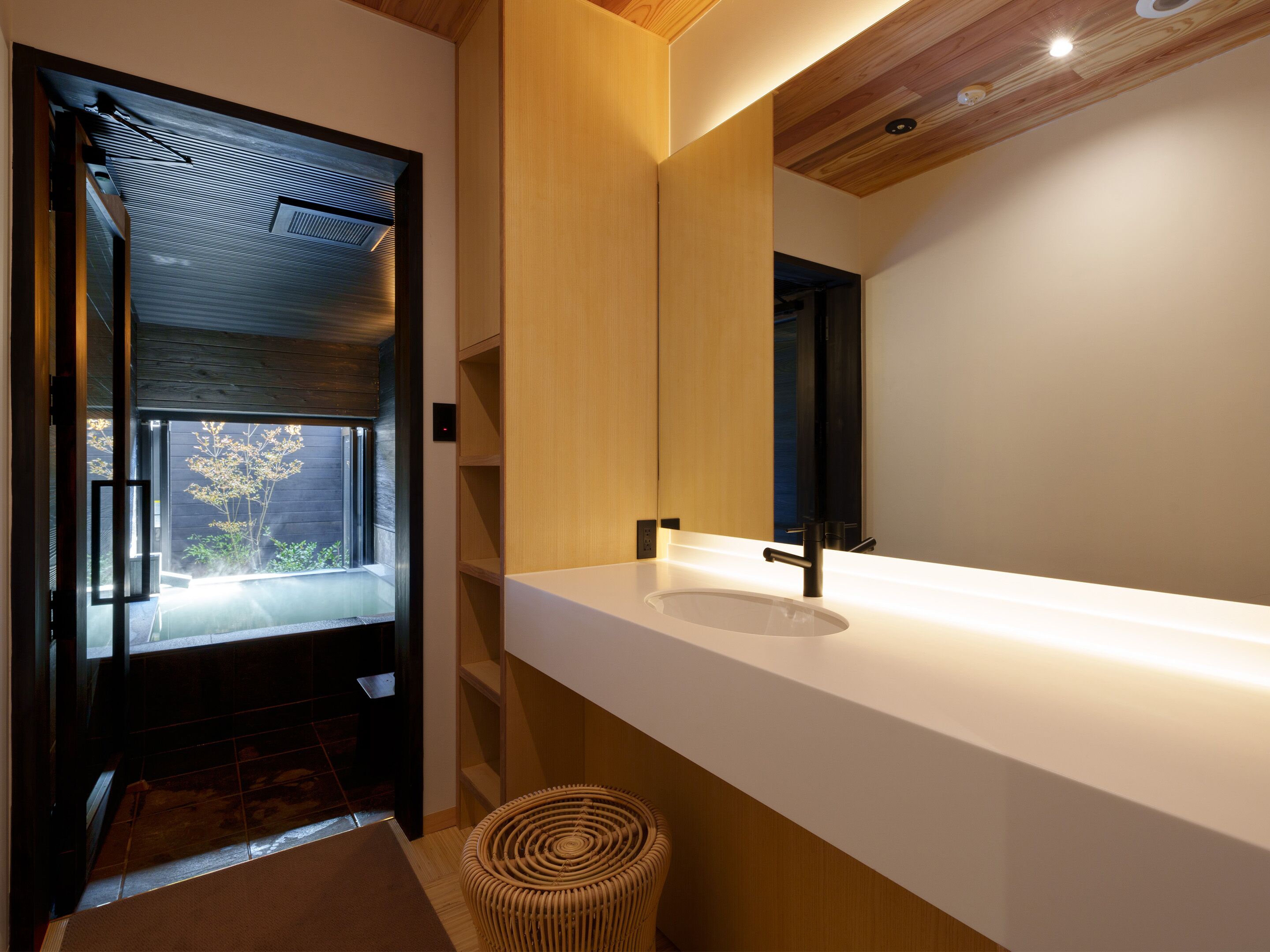 A modern bathroom with a large mirror, white countertop, and a wooden ceiling.