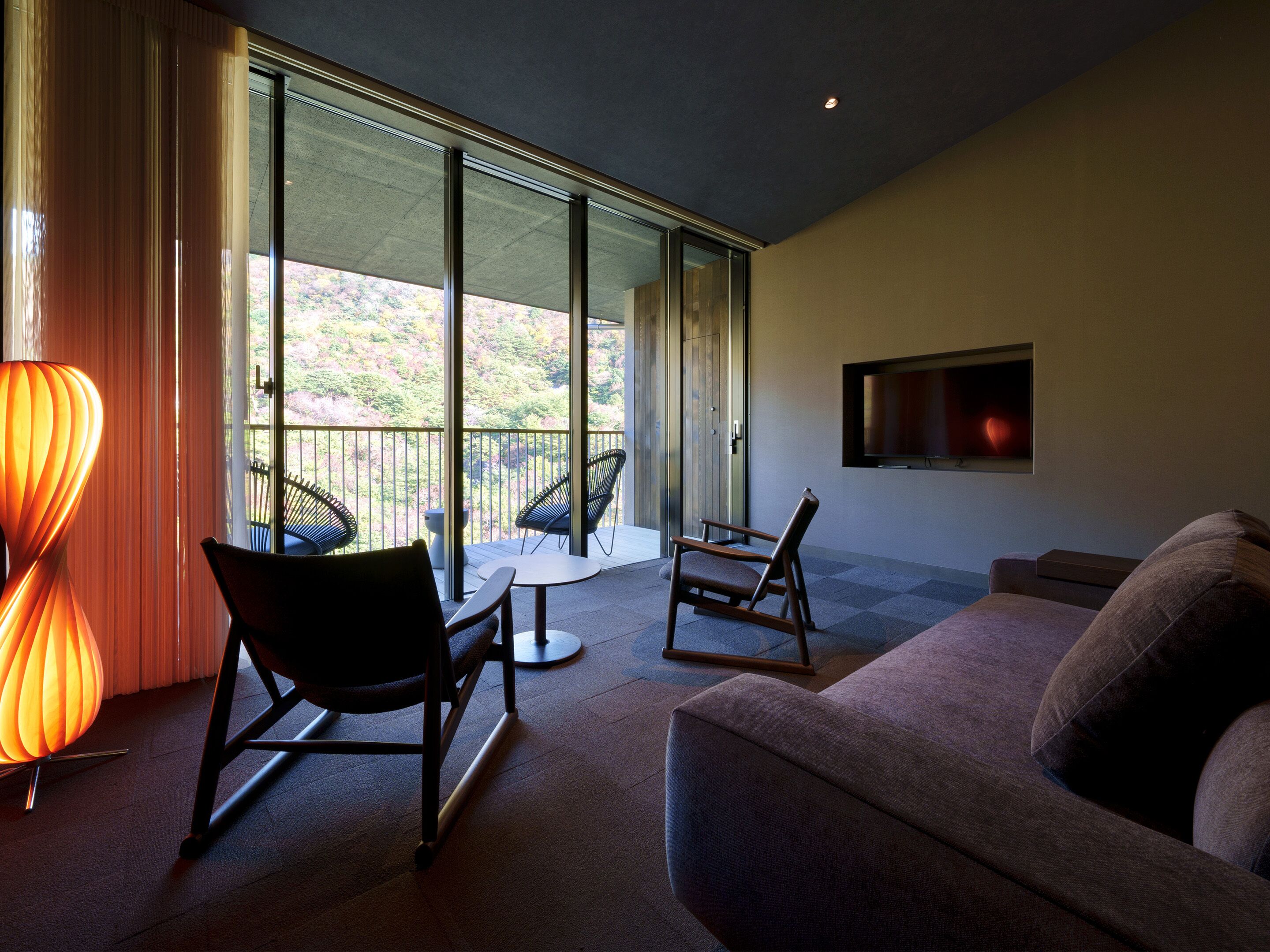 A modern living room with a sofa, two chairs, a table, and a TV mounted on the wall.