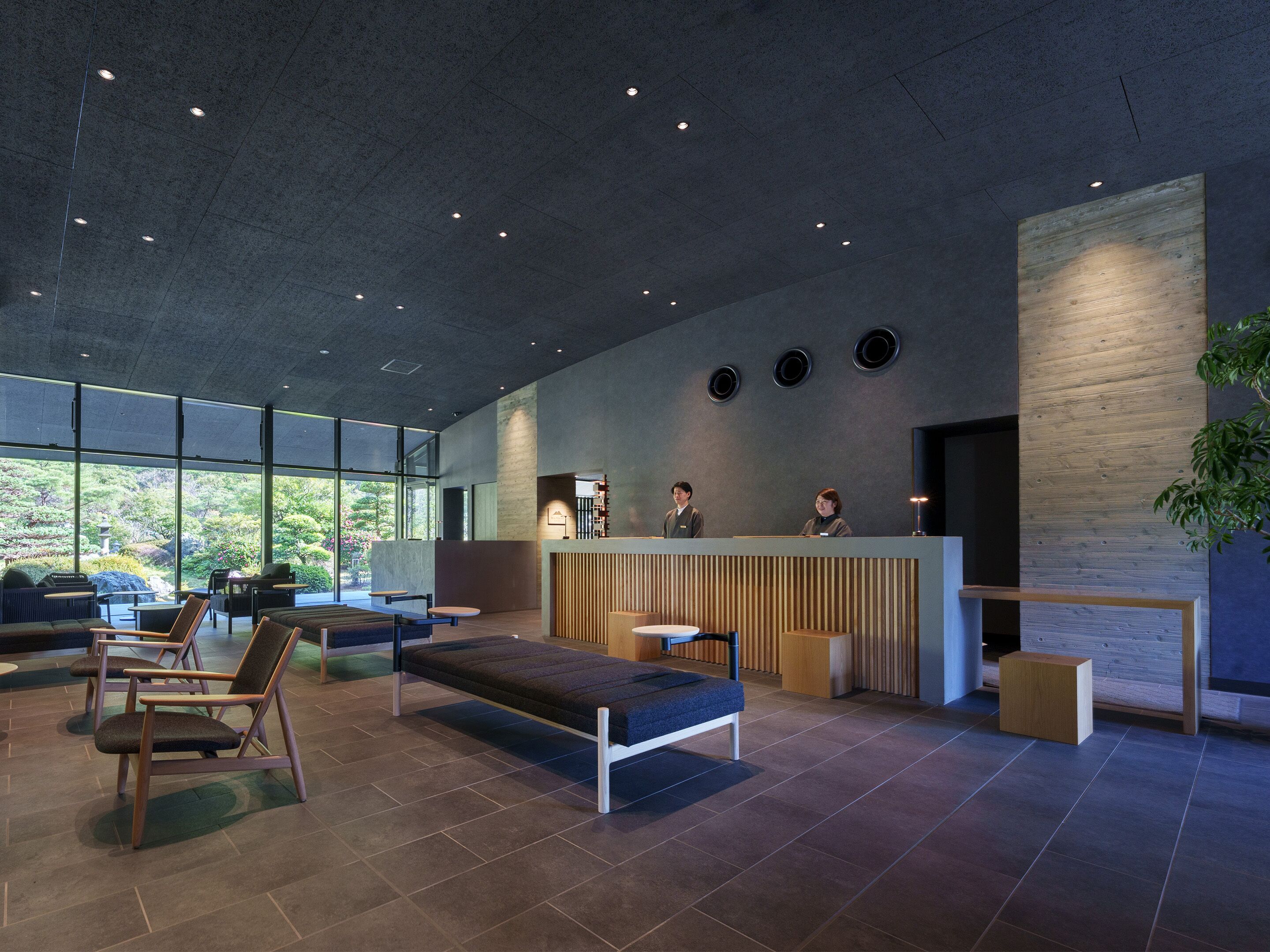 A modern reception area with a reception desk, seating, and large windows offering a view of greenery.