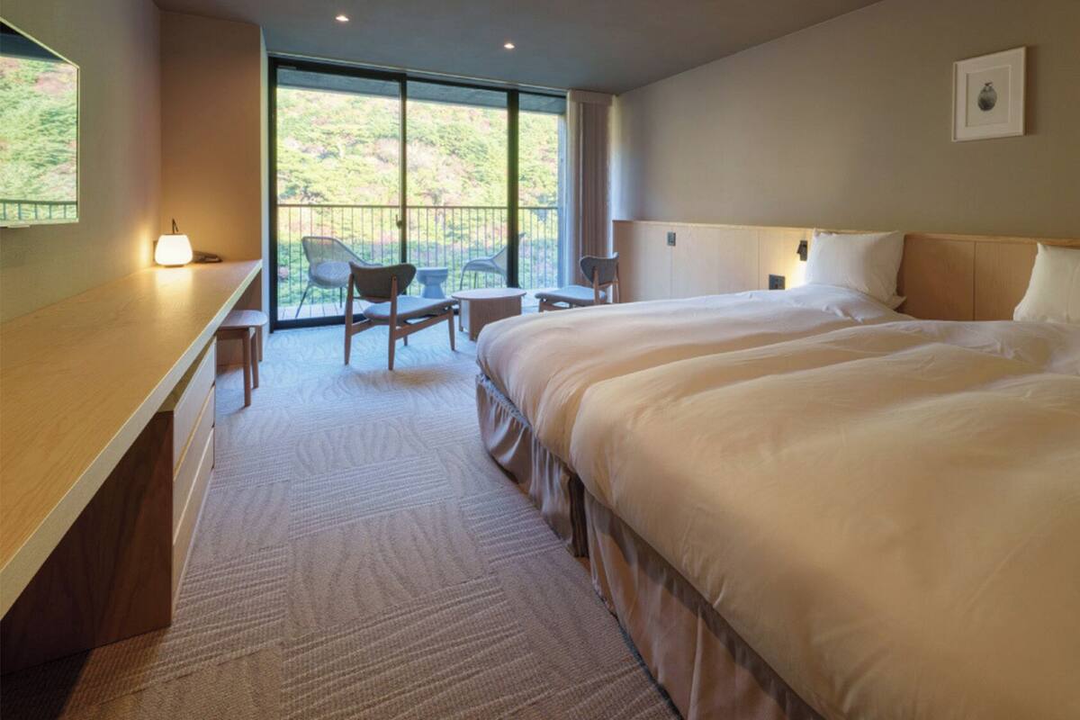 A hotel room with a large bed, a desk, a chair, and a balcony with a view.