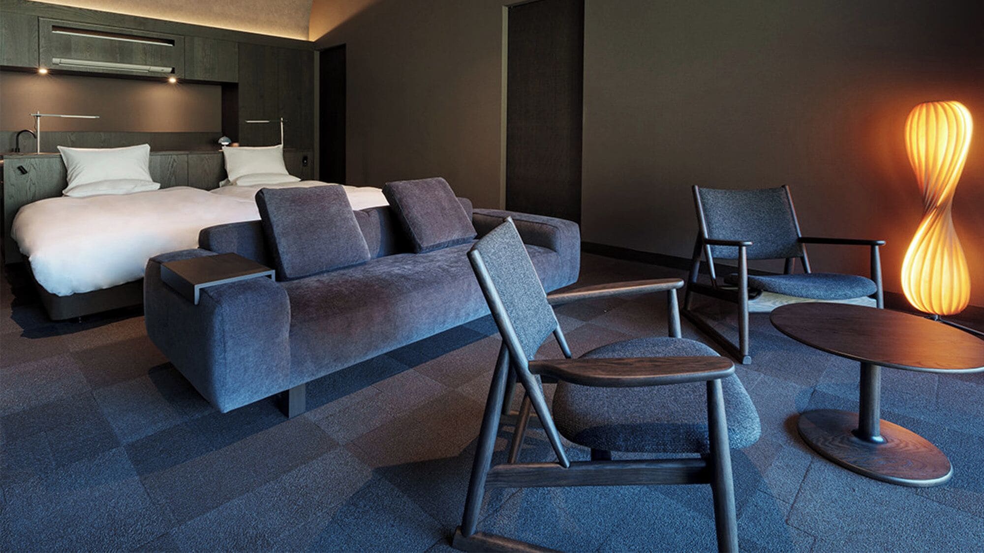 A modern hotel room with a bed, sofa, chairs, and a unique floor lamp.