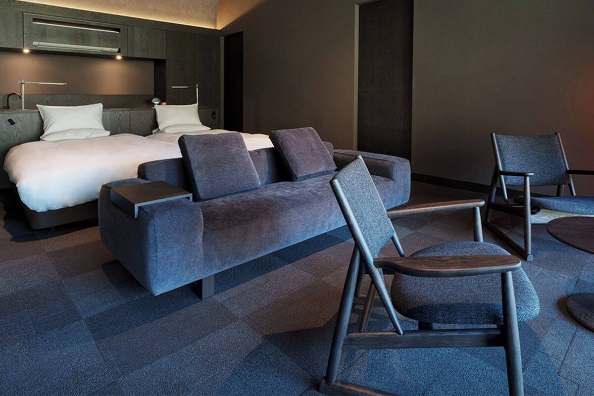 A modern hotel room with a bed, sofa, chairs, and a unique floor lamp.