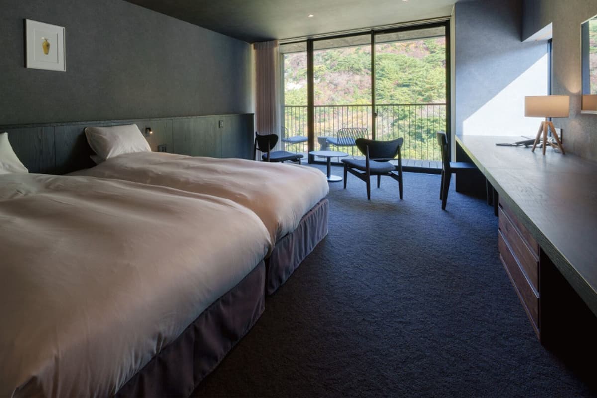 Ein Schlafzimmer mit einem großen Bett, einem Schreibtisch und einem Stuhl, mit Blick auf eine grüne Landschaft.