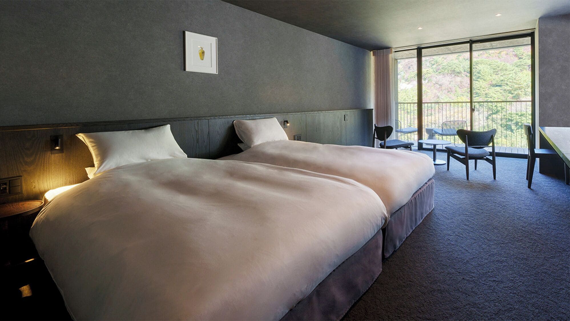 A double bed with a headboard, bedside tables, and a large window with a view of trees.