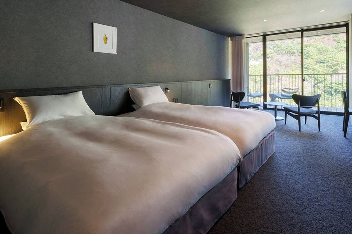 A double bed with a headboard, bedside tables, and a large window with a view of trees.