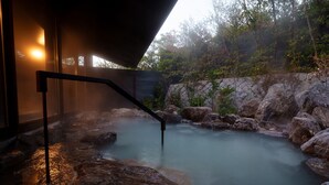 A hot spring area with a wooden deck and a stone wall. - Unzen Miyazaki Ryokan (Unzen)