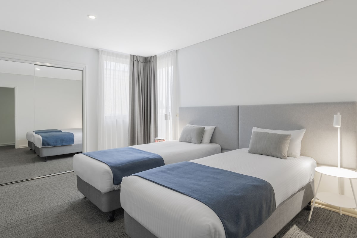 A hotel room with two beds, a large mirror, and a bedside table with a lamp.