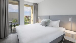 Moderni hotellihuone, jossa on suuri sänky, pieni pöyt ä ja parveke, jossa on ulkokalusteita.