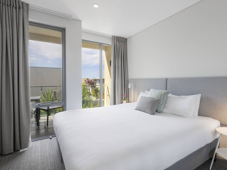 Ein modernes Hotelzimmer mit einem großen Bett, einem kleinen Tisch und einem Balkon mit Sitzgelegenheit.