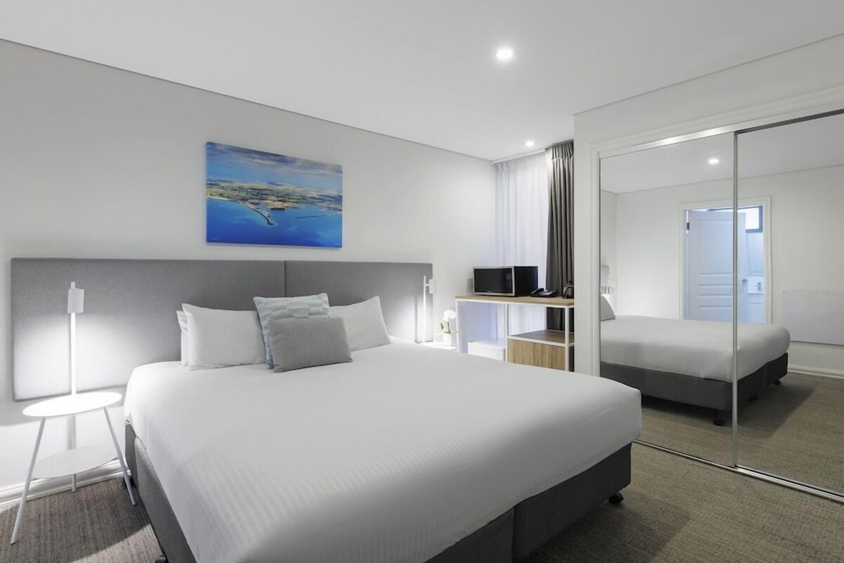 A modern hotel room with a large bed, a desk, a flat-screen TV, and a painting on the wall.