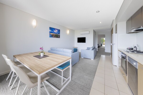 Un espacio habitable moderno con comedor, sofá, cocina y televisor montado en la pared.