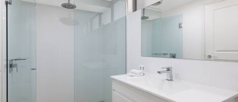 Un baño moderno con cabina de ducha de vidrio, tocador blanco con espejo y lavabo blanco.