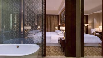 A hotel room with a large bathtub, a bed with white linens, a nightstand with a lamp, and a carpeted floor.