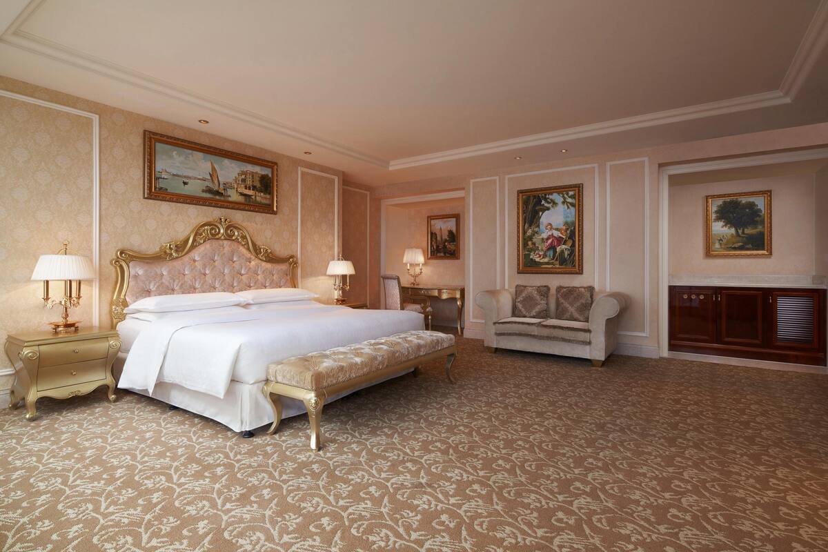 A spacious bedroom with a large bed, a bench, a nightstand, a chair, and a desk.