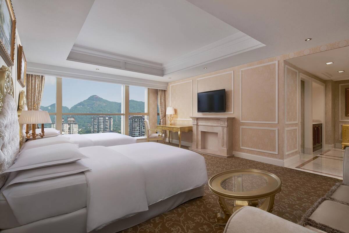 A hotel room with two beds, a television, a fireplace, and a view of a mountain.