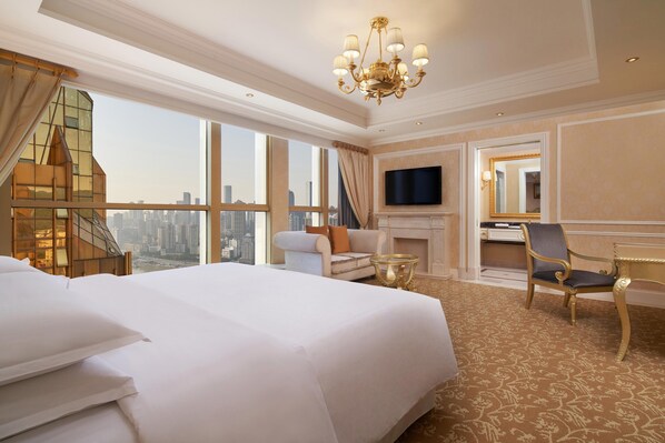 Habitación de hotel con una cama grande, televisión, chimenea, una silla y vistas a la ciudad.