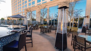 An outdoor patio with tables and chairs, a pool, and a tall, narrow fire feature.