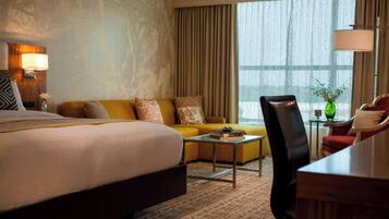 A hotel room with a large bed, a yellow sofa, a small table, and a chair.